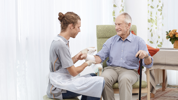 Ein FSW-Mitarbeiter verbindet einem Senioren den Arm mit einer Bandage