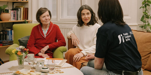 Eine FSW-Case-Workerin berät zwei Frauen an einem Wohnzimmer-Tisch