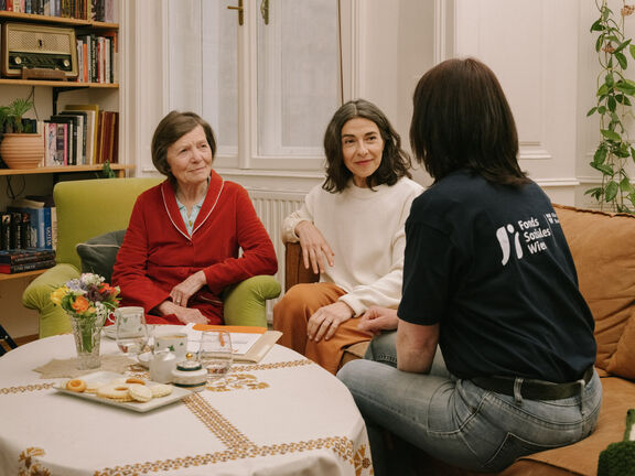 Eine FSW-Case-Workerin berät zwei Frauen an einem Wohnzimmer-Tisch