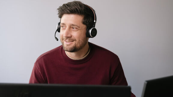 Ein junger Mann trägt ein Headset, sitzt auf einem Arbeitsplatz und blickt nach links
