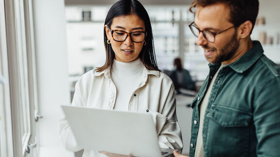 Eine Frau mit schwarzen Haaren und ein Mann mit Jeans-Hemd schauen auf einen Laptop