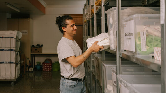 Ein FSW-Mitarbeiter schlichtet Handtücher in ein Regal in einer Wohneinrichtung