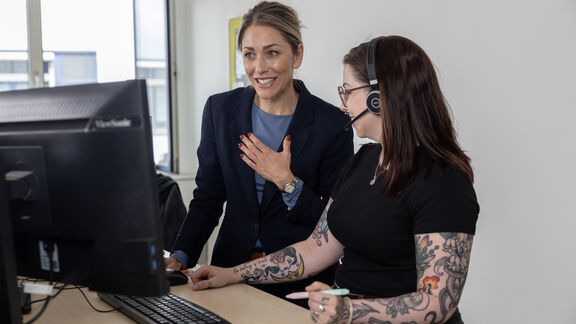 Zwei FSW-Mitarbeiterinnen stehen an einem Arbeitsplatz vor einem Computer und besprechen etwas