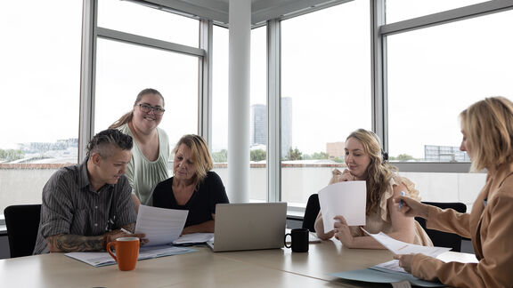 Fünf FSW-Mitarbeiter:innen sind in einem Besprechungsraum und besprechen Dokumente