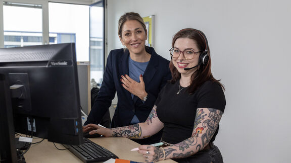 Zwei FSW-Mitarbeiterinnen stehen an einem Arbeitsplatz vor einem Computer und besprechen etwas